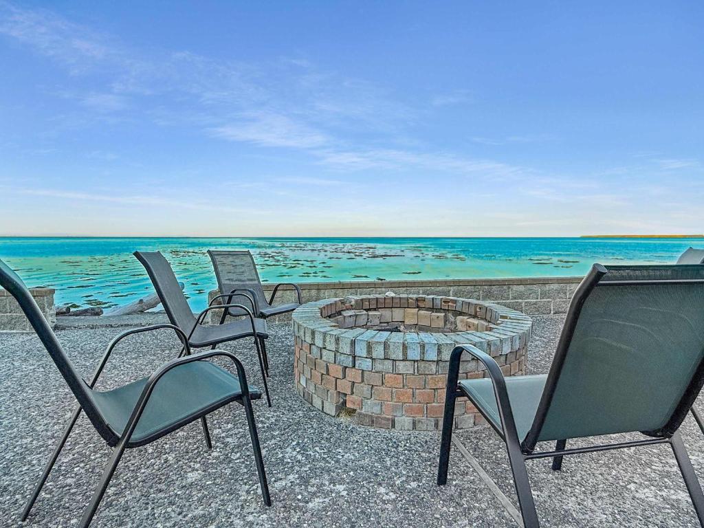 three chairs and a fire pit on the beach at Sq Seaside Cottage in Sequim