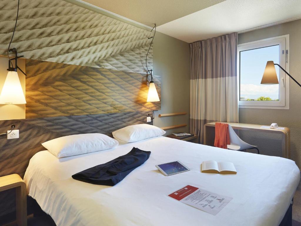 a hotel room with a large bed with two books on it at ibis Archamps Porte de Genève in Archamps