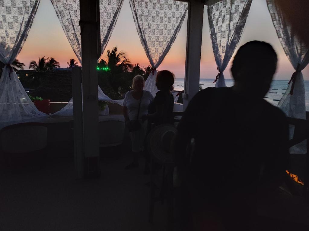 a group of people sitting at a table watching the sunset at Nils Home in Nungwi