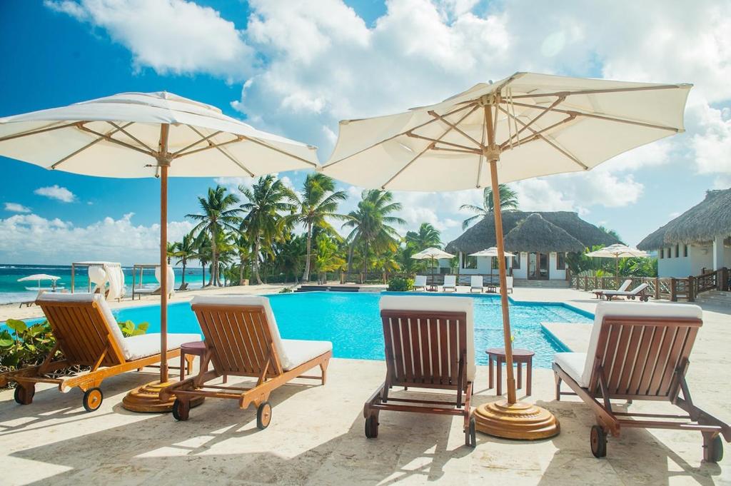 a group of chairs and umbrellas next to a pool at 1 Bedroom Apartment with spectacular pool and golf course view in Punta Cana