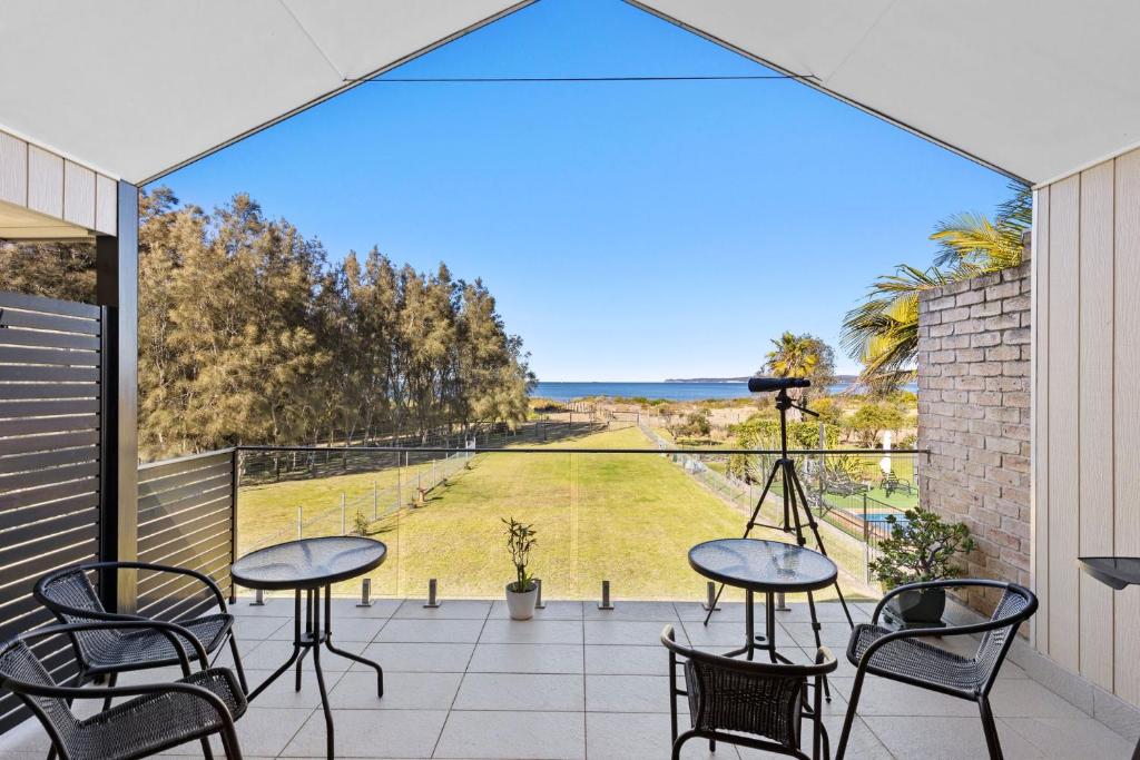 Un balcón con mesas y sillas y vistas al océano. en Sandy Place Beach House managed by Batemans Bay Accom, en Long Beach