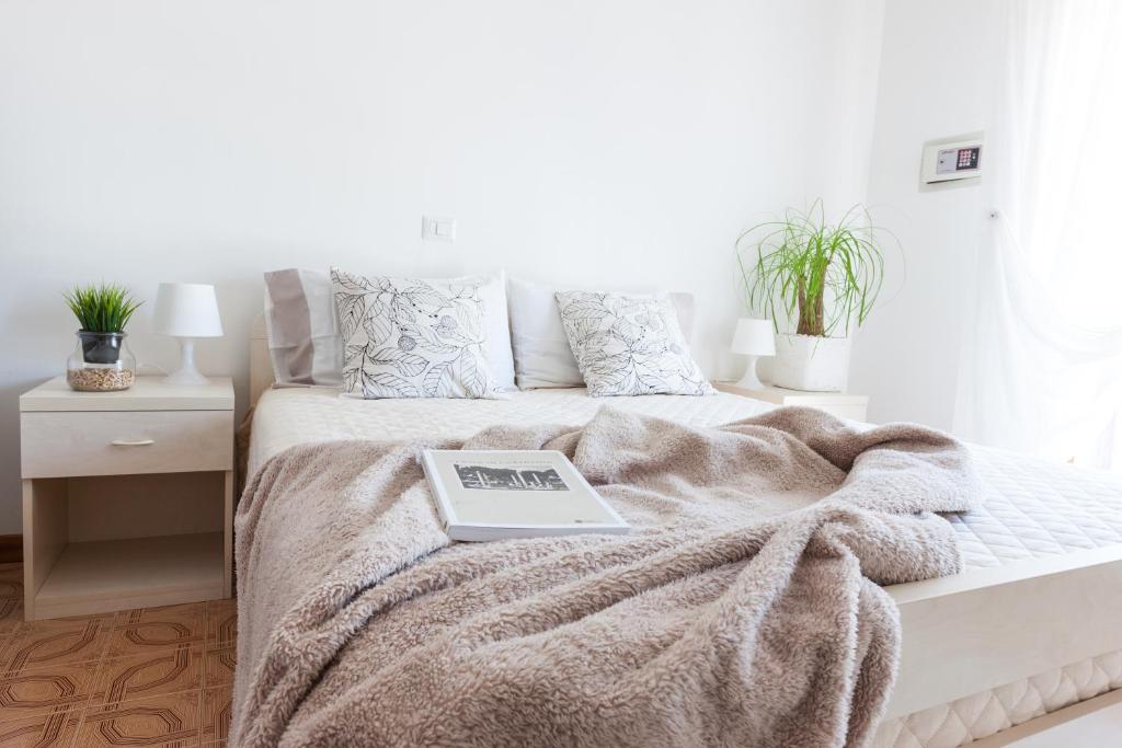 a white bedroom with a bed with a book on it at Villa dei Fiori Apartments in Cervia