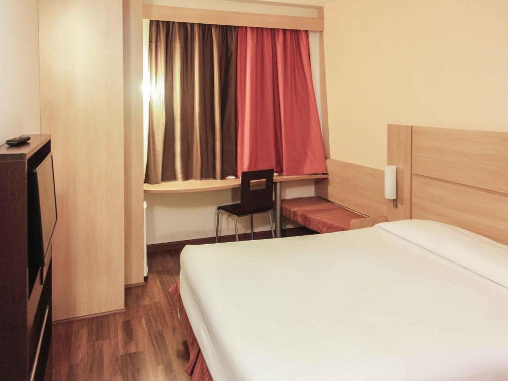 a bedroom with a bed and a desk and a window at Ibis Sertaozinho in Sertãozinho
