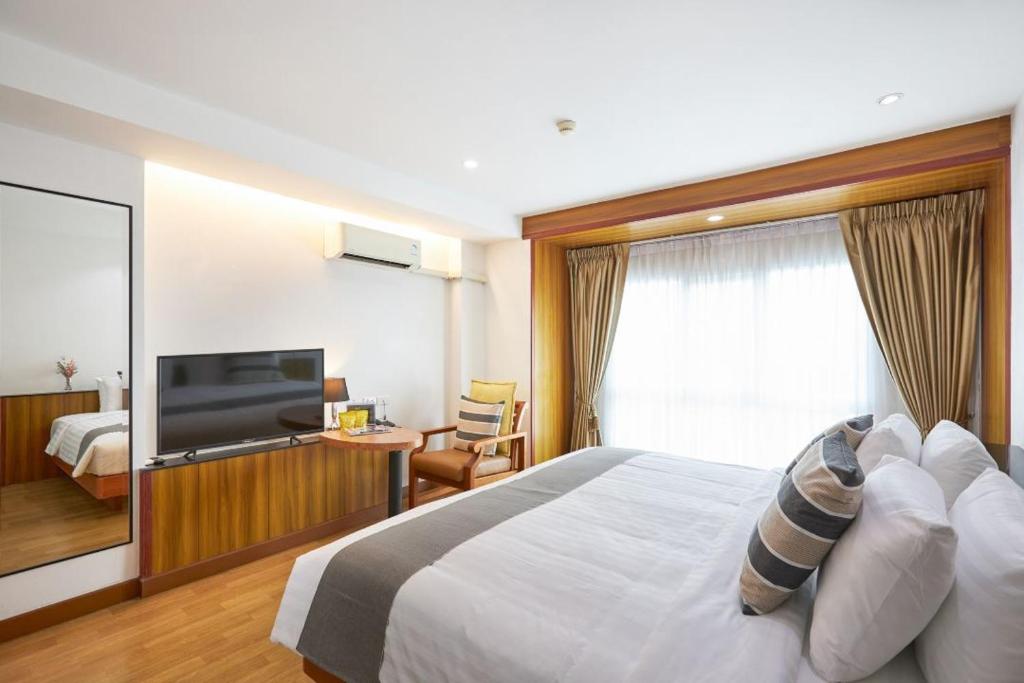 A bright guest room with a large bed, television, armchair, and full-height curtained window.