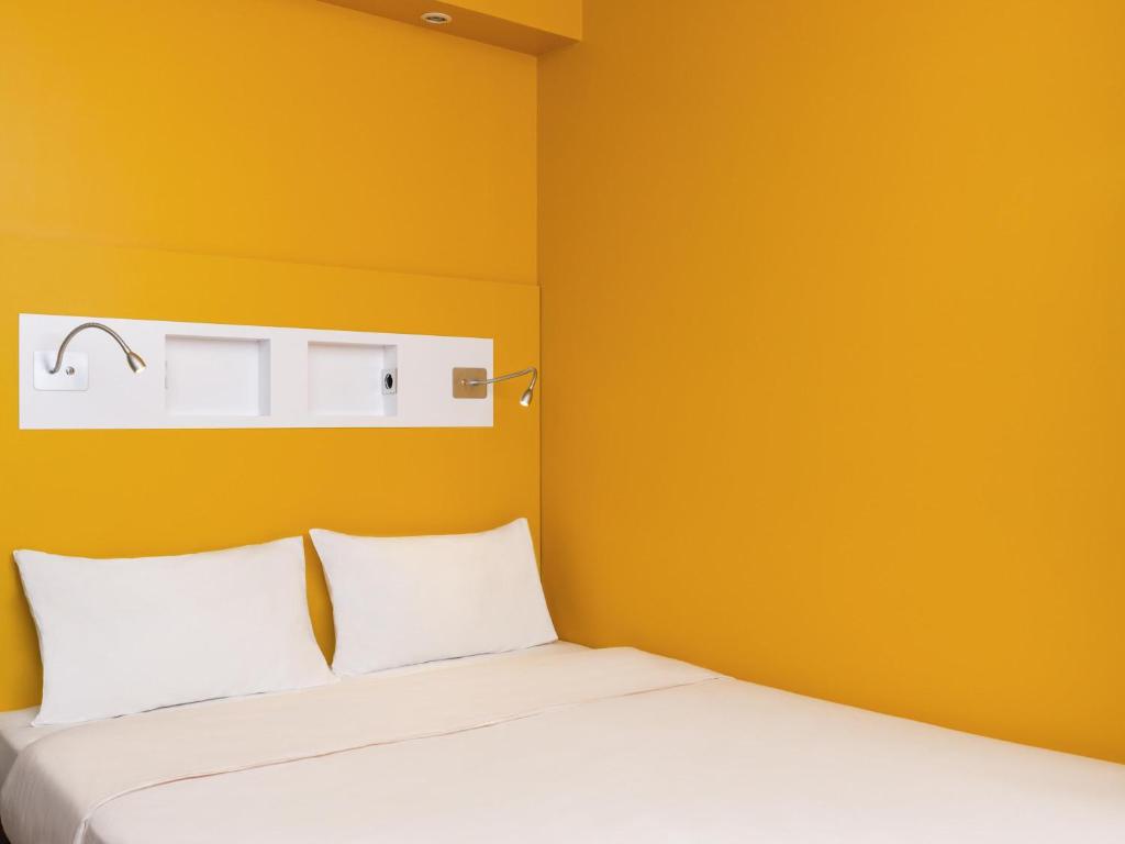 a bedroom with yellow walls and a bed with white pillows at ibis budget Rouen Nord Isneauville in Isneauville