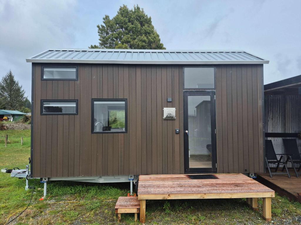 a brown tiny house with a wooden deck at Rimu View 3 by Tiny Away in Ruatapu