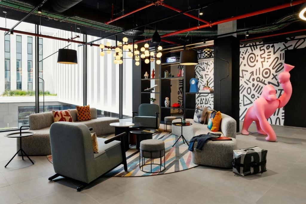 A bright communal lounge offers varied seating beside tall windows and playful artwork.