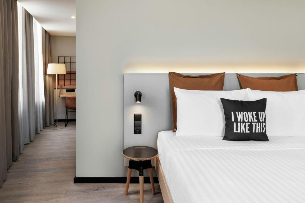 A double bed sits beside a small round table, with a desk visible along the curtained window wall.