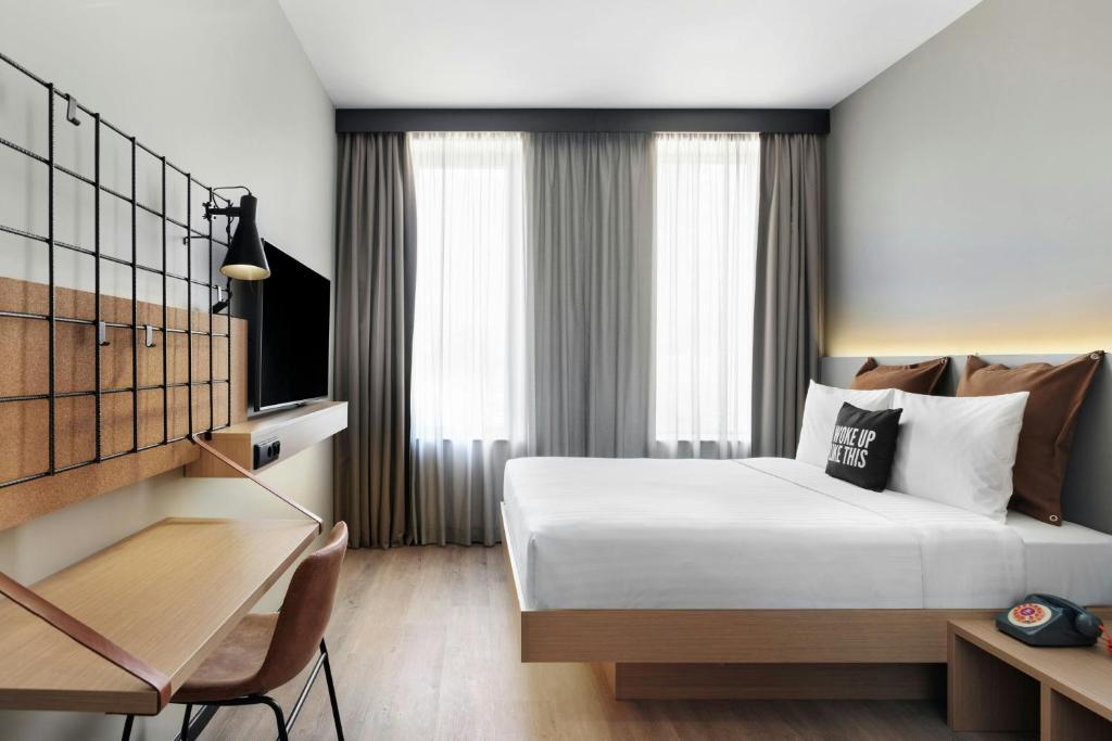 A compact in-room desk beside the bed, with a laptop, television, and bright curtained windows.