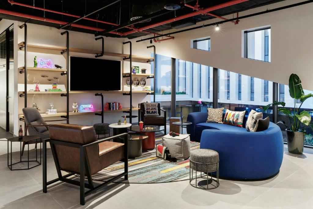 A bright hotel lounge with a blue curved sofa, armchairs and large windows.