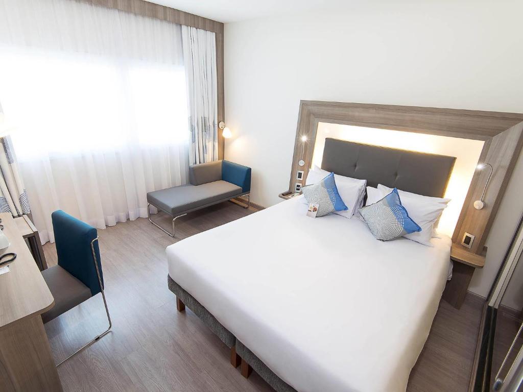 a bedroom with a large white bed and a chair at Novotel Santos Gonzaga in Santos