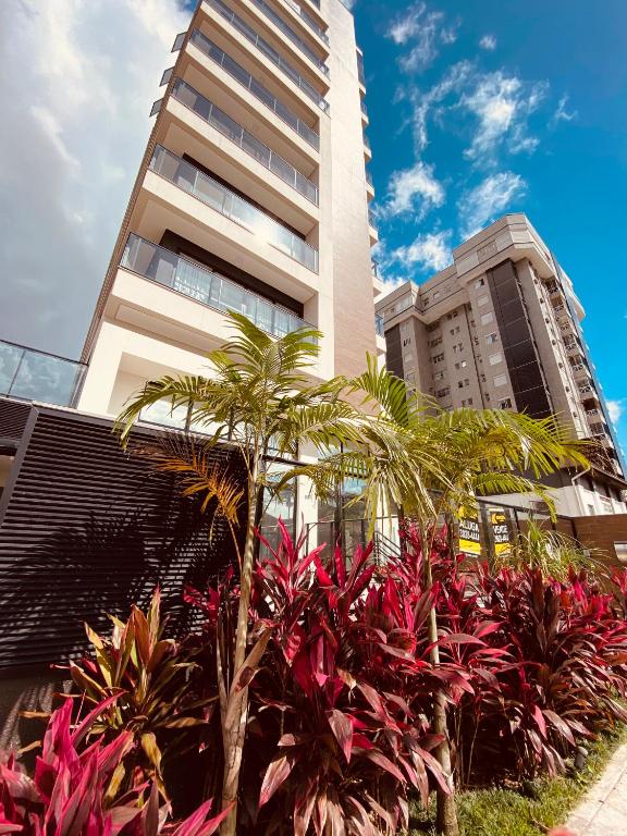 a tall building with palm trees in front of it at MaxLoft apto completo cozinha e lavanderia in Joinville