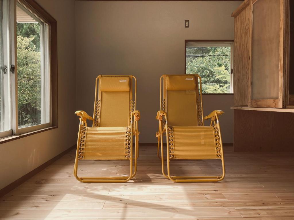 deux chaises dans une pièce avec deux fenêtres dans l'établissement 森と温もりに包まれる長野飯綱高原の隠れ宿ヴァイオレットハウス, à Nagano