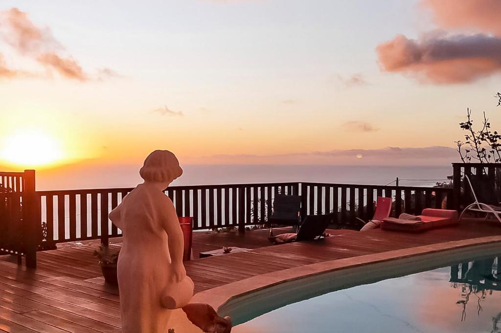 una donna in piedi accanto a una piscina con il tramonto di KAZ PANORAMA Luxe Créole Piscine et Terrasse Vue Panoramique Océan Fruits du Jardin Parapentes a Saint-Leu
