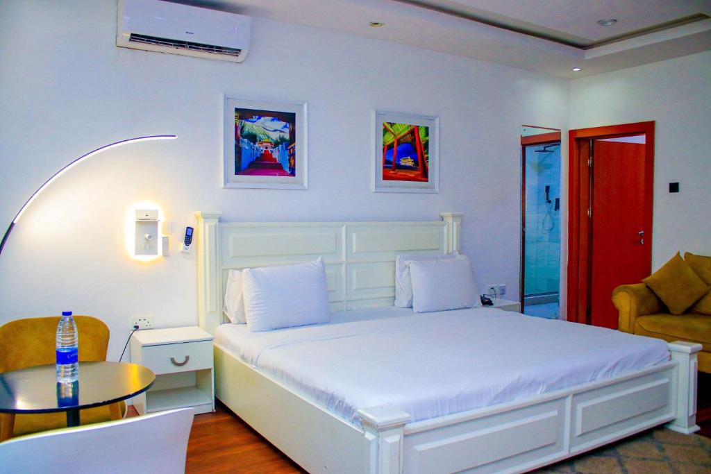 a white bedroom with a bed and a table at The Glass Residence Jabi in Abuja