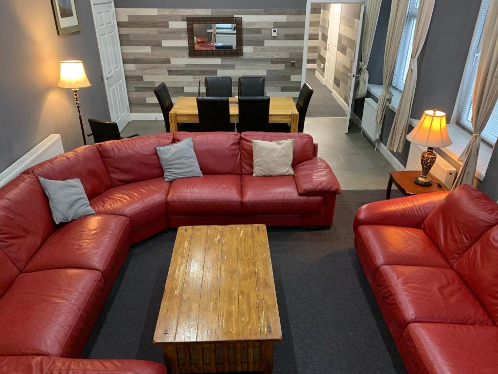 a living room with a red leather couch and a table at Spacious Holiday let midway between Edinburgh and Glasgow with three shower rooms in Kirk of Shotts