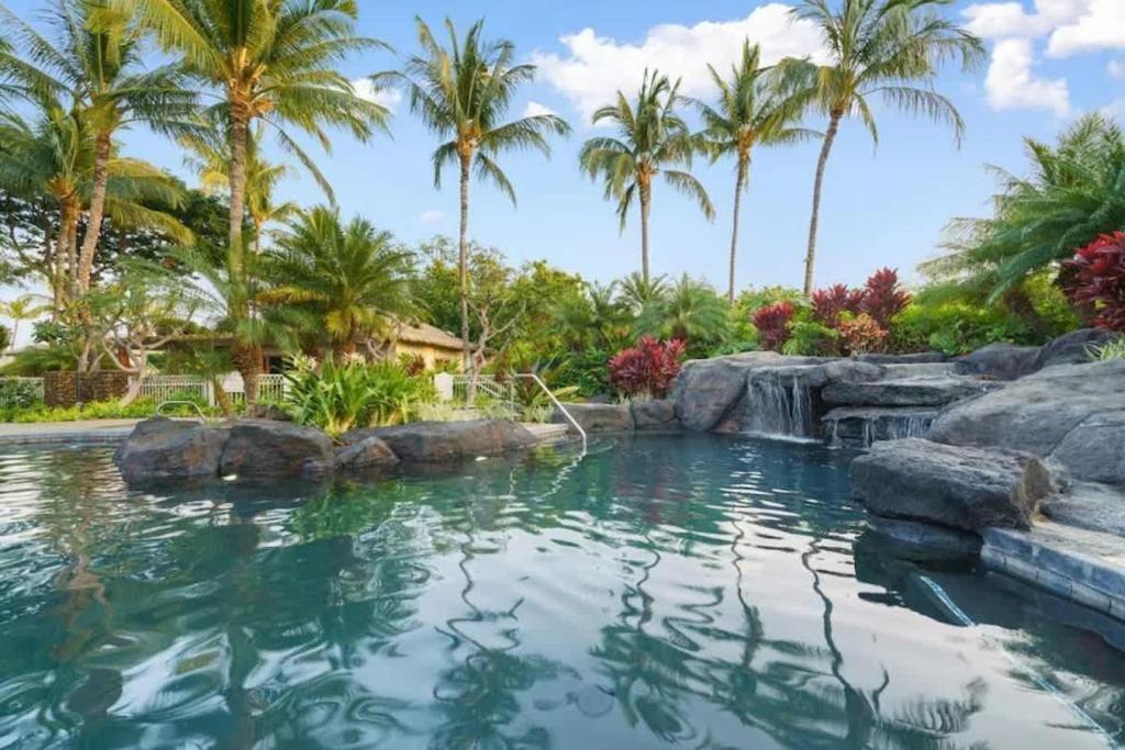 une piscine avec une cascade et des palmiers dans l'établissement Luxurious Mauna Lani Condo with Private Beach Club Access, à Waikoloa