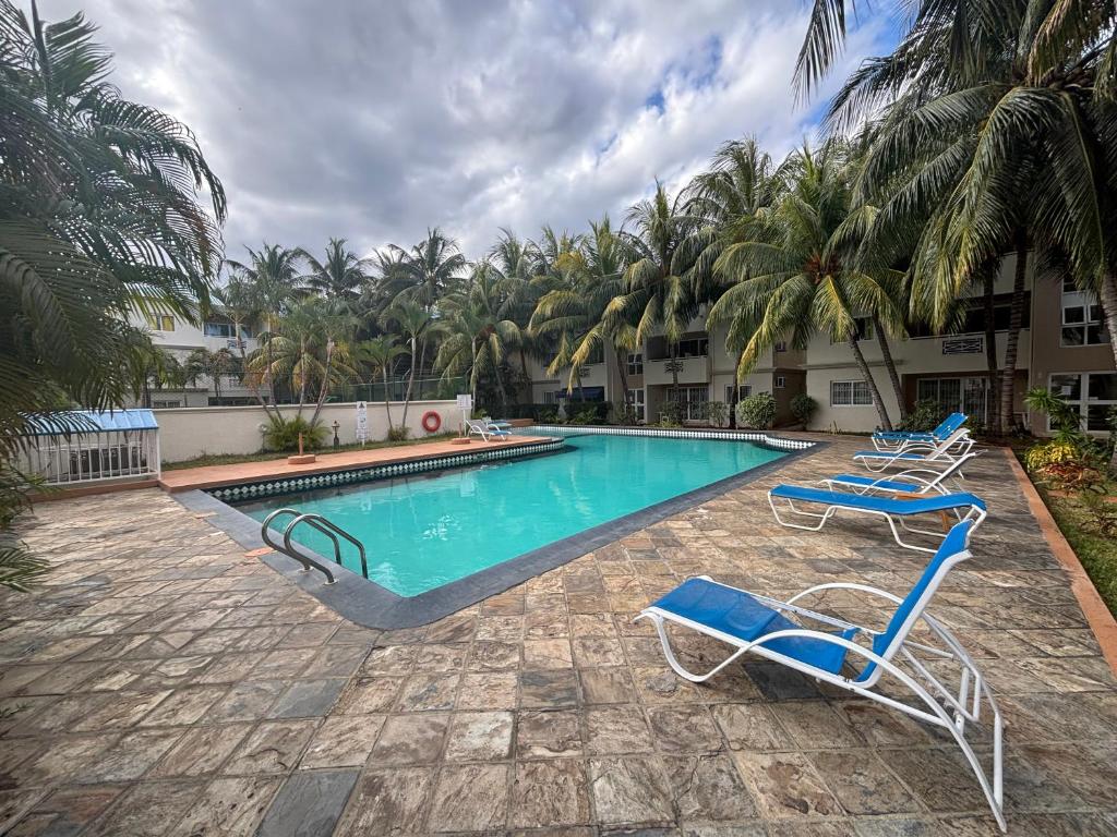 a swimming pool with two blue chairs and palm trees at Charming Apartment with Pool View Near the Beach in Flic-en-Flac