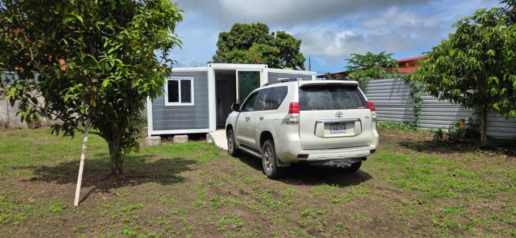 Una camioneta blanca estacionada frente a una pequeña casa en contenedor estudio, en Tilarán