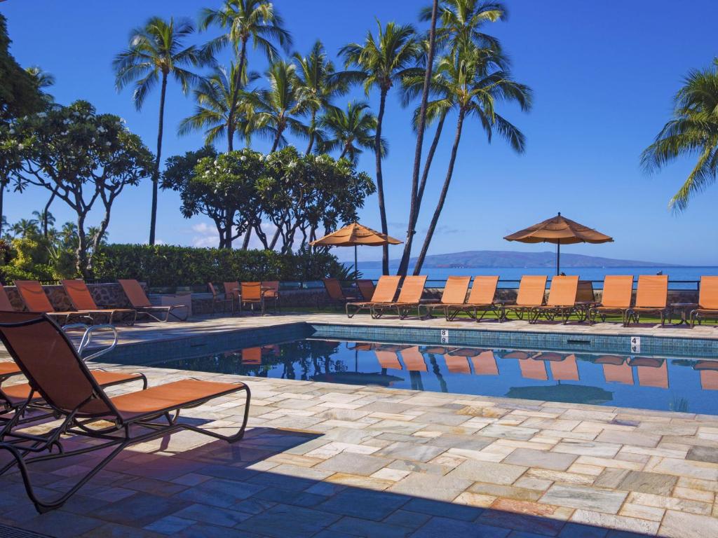 a swimming pool with chairs and palm trees and the ocean at Wailea Elua Village 1102 in Wailea