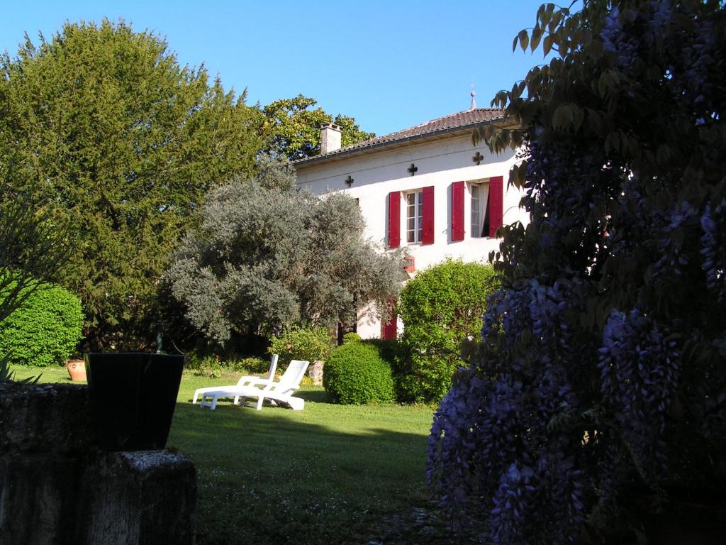 a white house with red shutters and a white chair in the yard at A L'Olivier in Montcaret