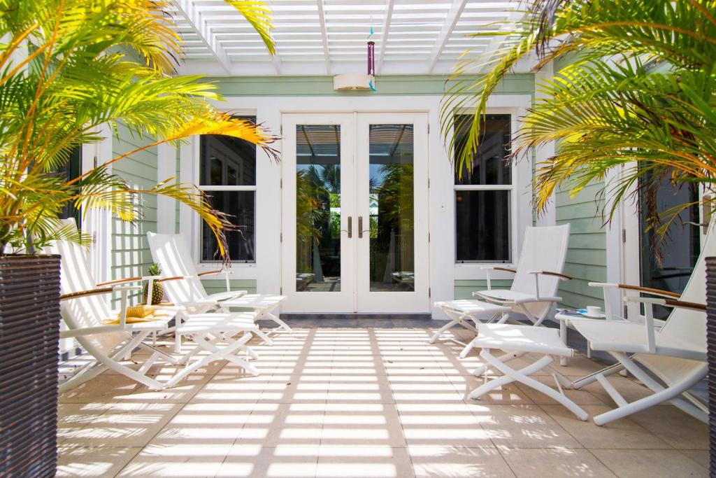a patio with white chairs and palm trees on a house at Pomegranate Cottage in West Bay