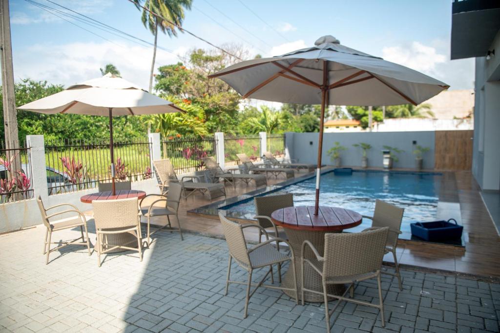 two tables and chairs with umbrellas next to a pool at Apto com 2 Suites, Piscina e Jogos a 100m da praia in São Bento