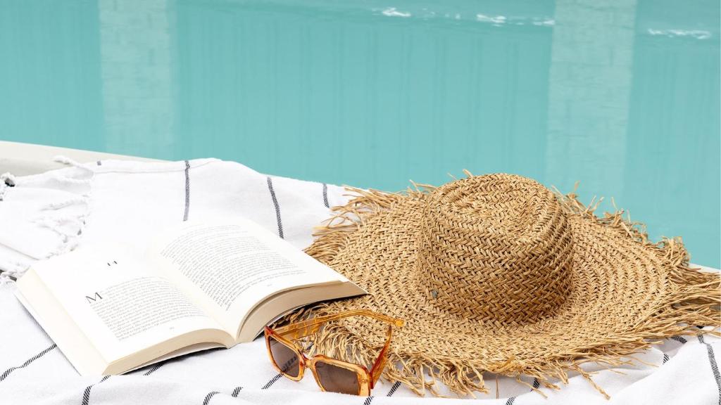 a straw hat and glasses and a book on a bed at Pandanus - Spacious Waterfront Escape with Private Pontoon & Pool - Holiday Yamba in Yamba