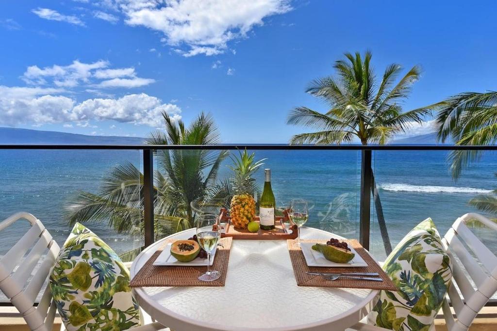 a table with food and wine on a balcony with the ocean at Mahana 602 · MA 602 Kaanapali OceanFront Studio Ocean View Pool in Kahana