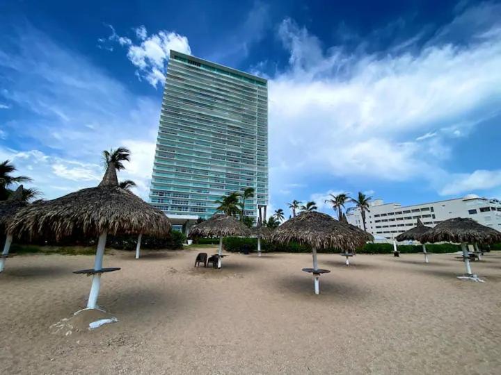 a beach with straw umbrellas and a tall building at Beachfront Apartment in Mazatlán