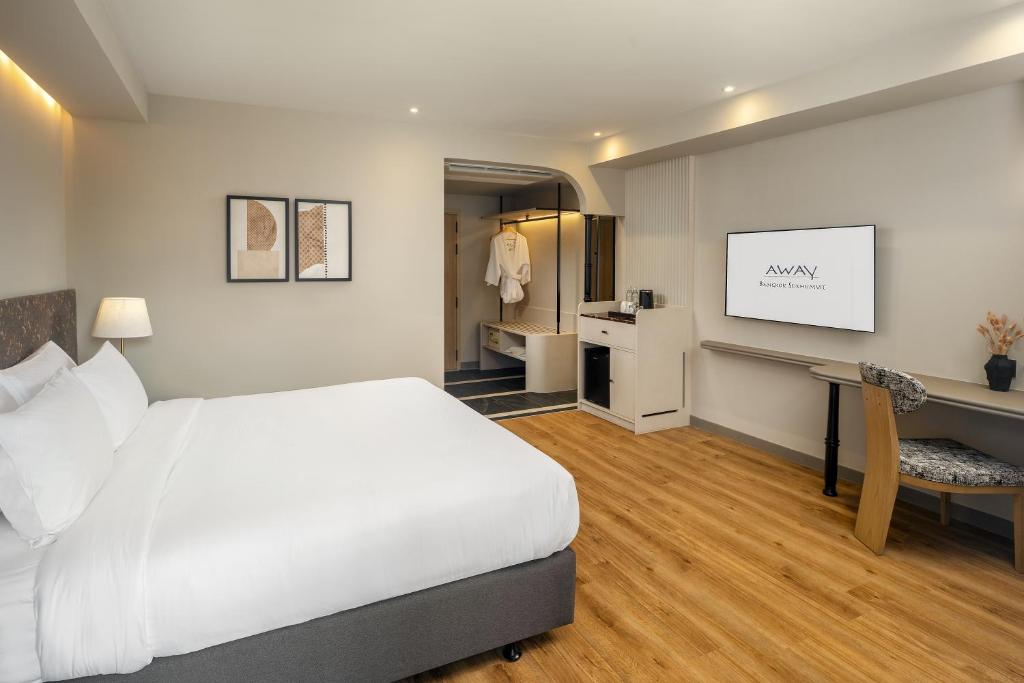 A bright bedroom with a large bed, wall-mounted television, desk and open wardrobe.