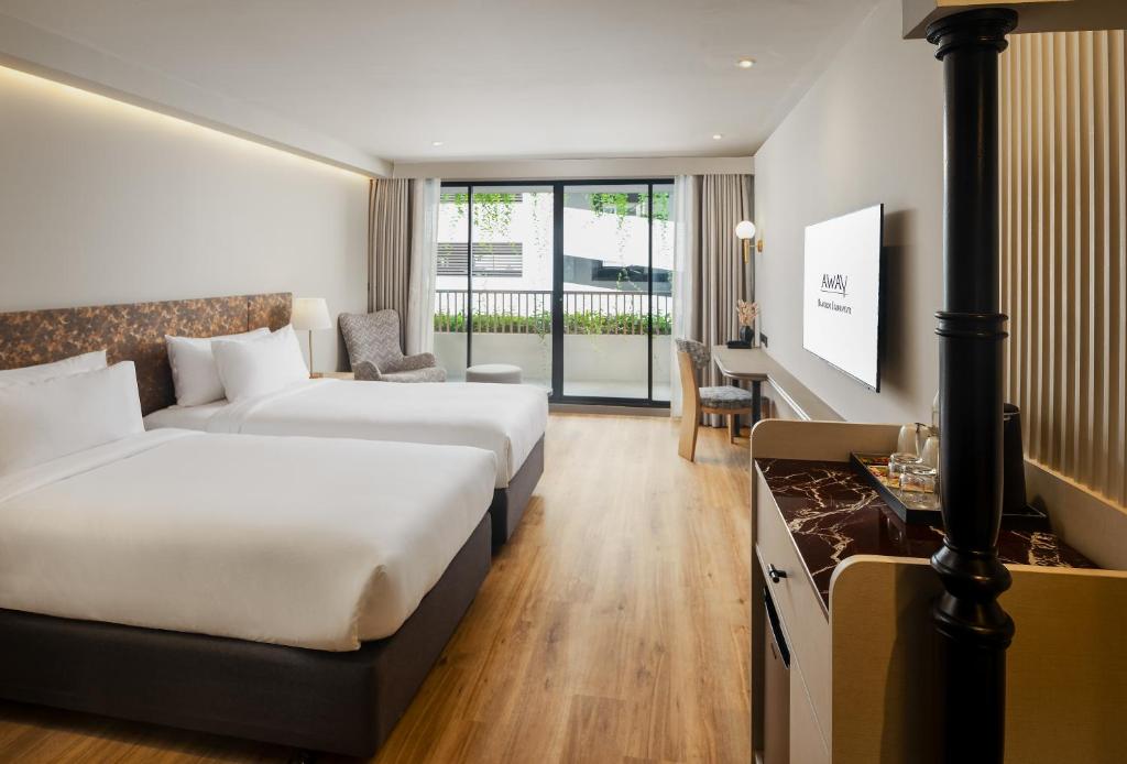 A twin room with two beds, a desk and a full-height glazed opening to greenery and nearby buildings.