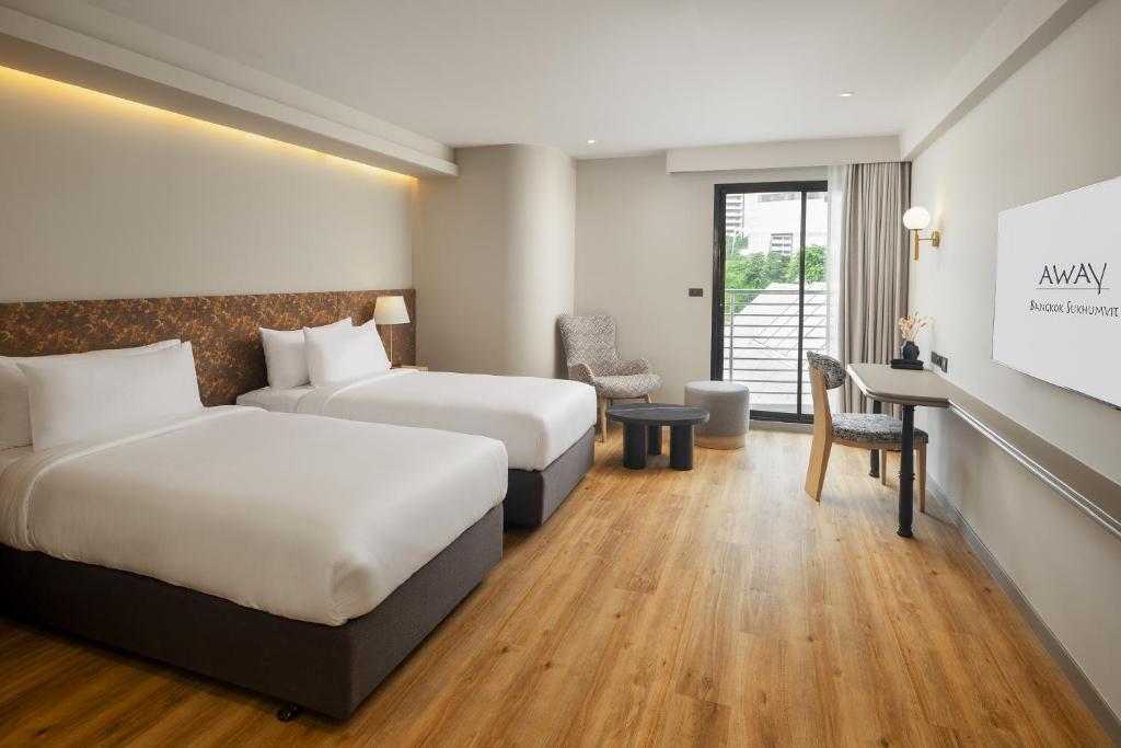 A twin room with two beds, a compact work desk and a glazed opening beside a lounge chair.