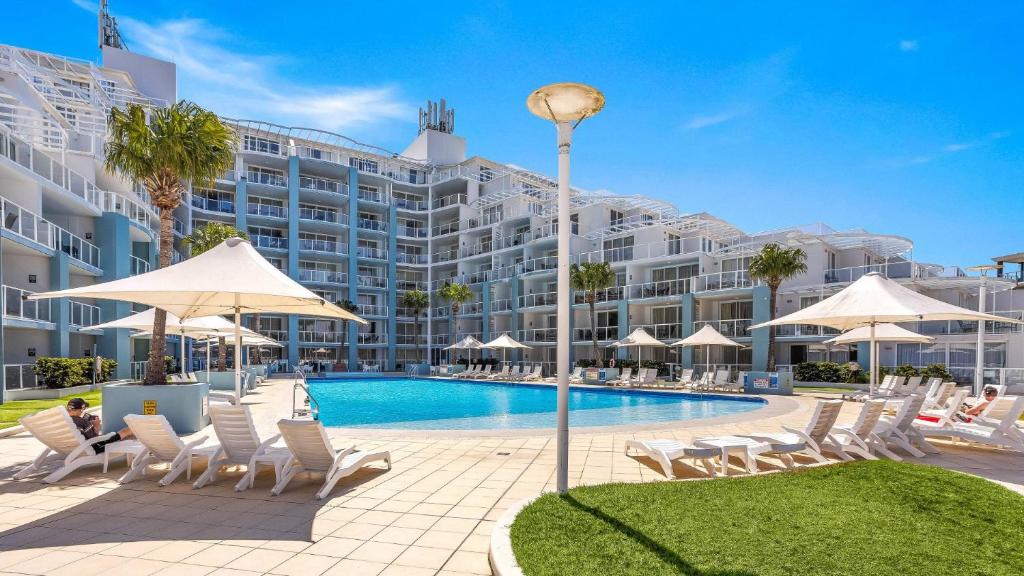 a hotel with a pool and chairs and umbrellas at Allure in Ettalong Beach
