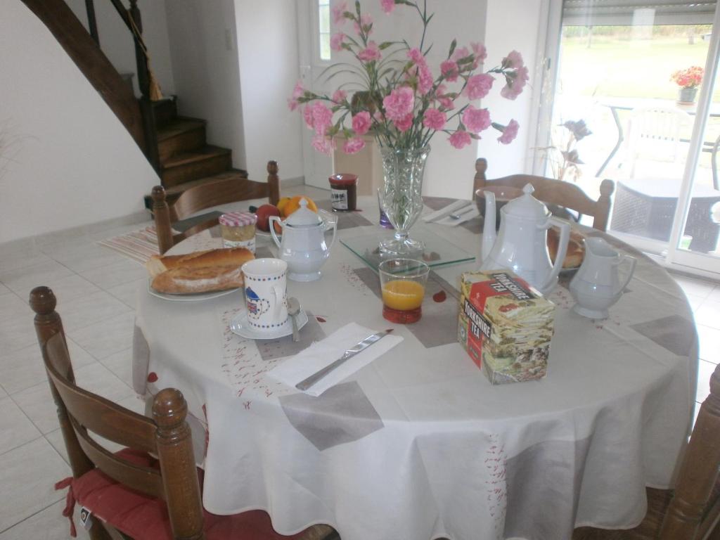 una mesa con mantel blanco y una mesa con comida y flores en Chambre d'hôtes La Haie en Roz-Landrieux