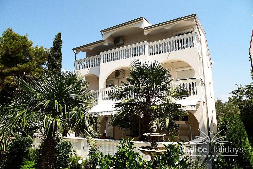 a large white building with palm trees in front of it at Amelia Apartment in Vodice