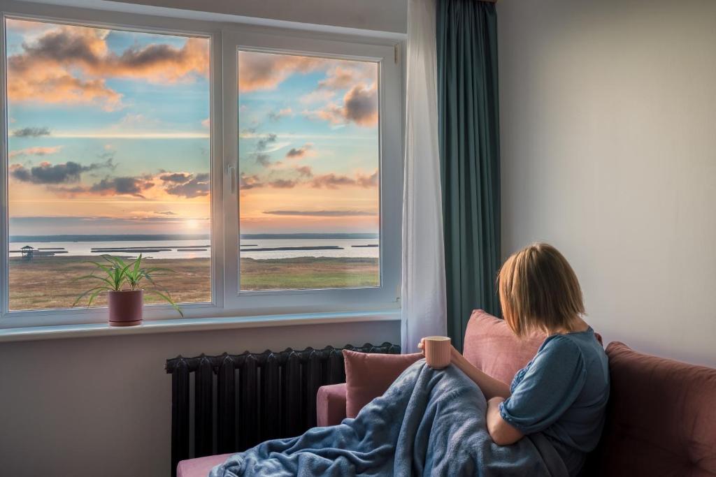 una mujer sentada en un sofá mirando por una ventana en Lakeview stay, stunning sunrises, en Liepāja