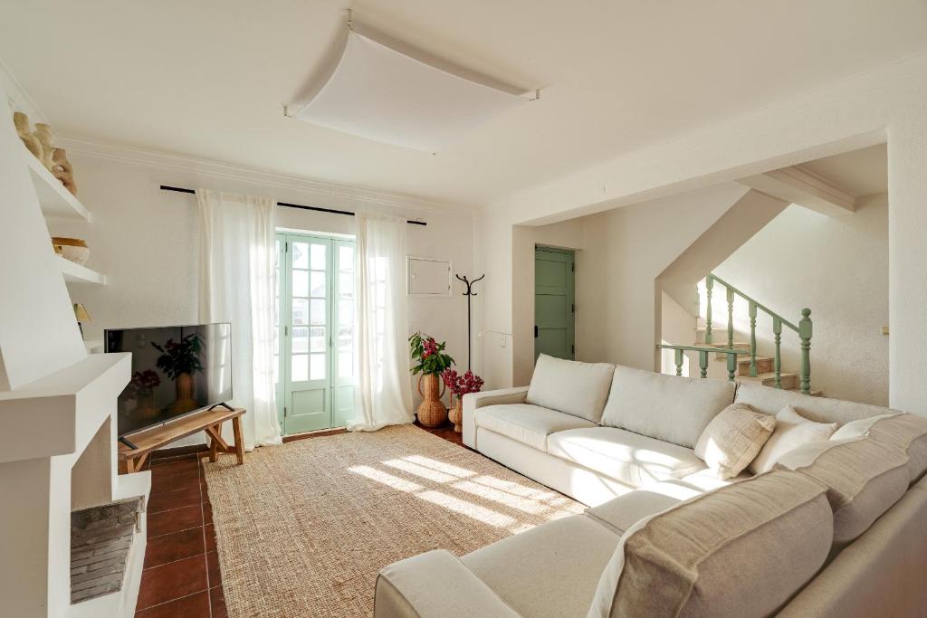 ein Wohnzimmer mit einem weißen Sofa und einem Fernseher in der Unterkunft Charneca Caparica Casa Rey by Hopstays in Vale de Cavalos