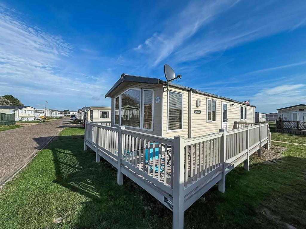 a white house with a porch on the grass at Lovely Caravan With Spacious Decking At North Denes In Suffolk, Ref 40134Nd in Lowestoft