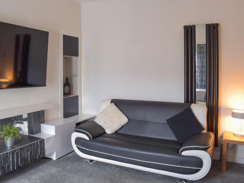 a living room with a black leather couch and a tv at Greens Cottage in Girvan