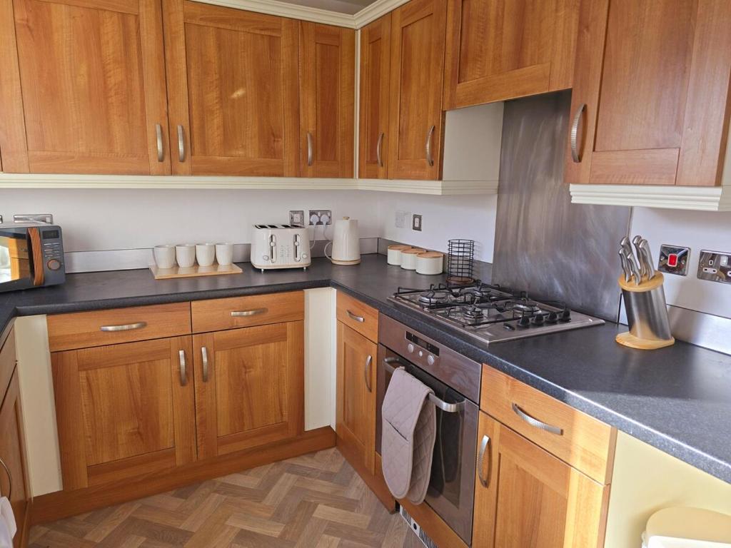 a kitchen with wooden cabinets and a stove top oven at Family-Friendly 4-Bed Swansea Stay with Parking in Landore