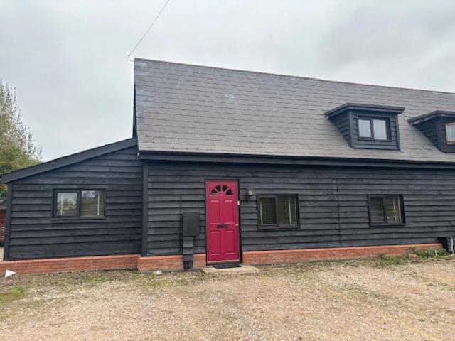 a black house with a red door and windows at 2 Willow Cottage in Takeley