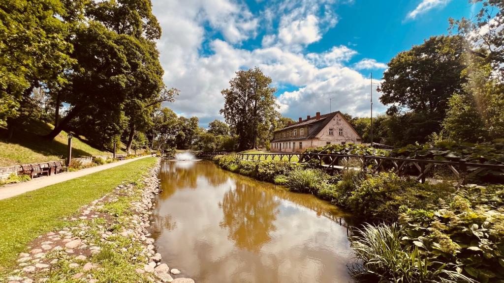 a river in a park with a building in the background at Pils Parka Apartamenti in Kuldīga