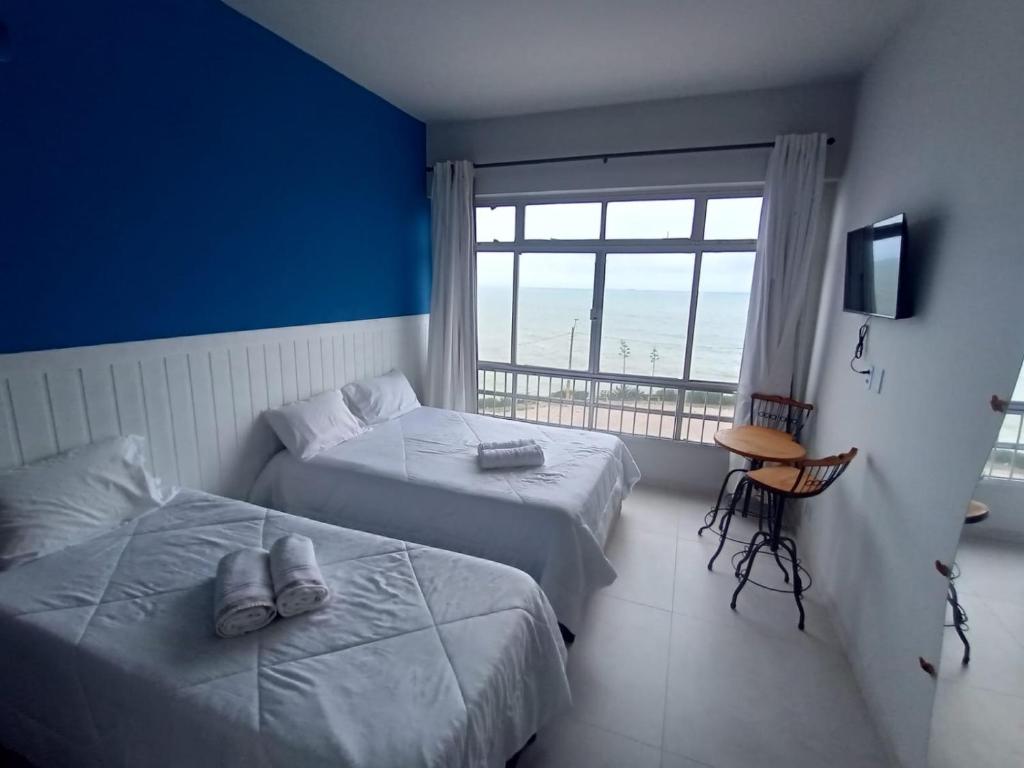 two beds in a room with a large window at Mirante do Ipiranga Apartment in Guarapari