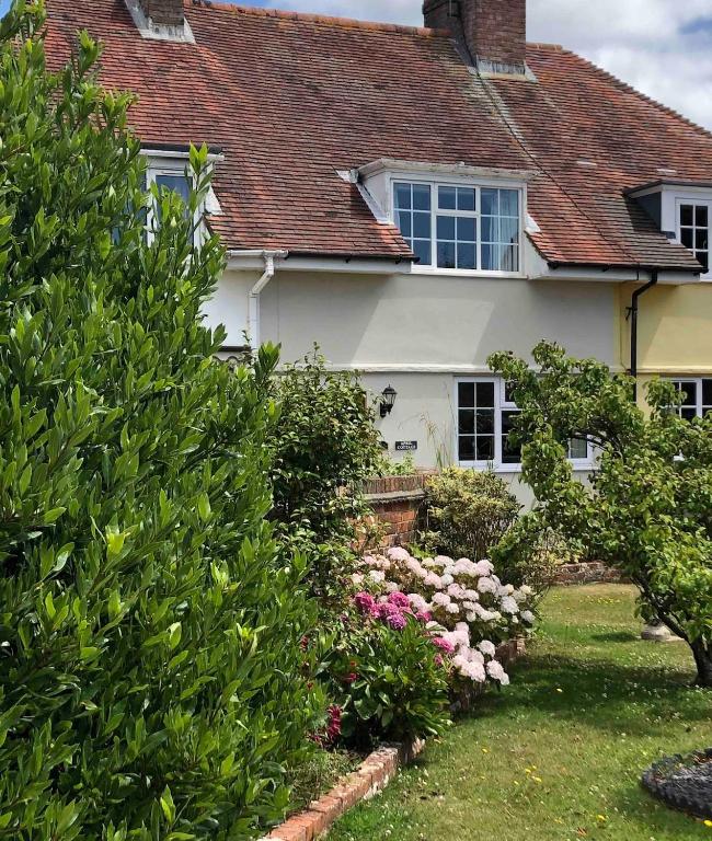a white house with bushes and flowers in the yard at April Cottage in Lymington
