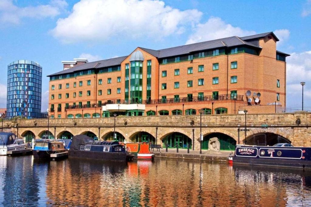 シェフィールドにあるSandman Signature Sheffield Quays Hotelのボートのある川のそばにある大きなレンガ造りの建物