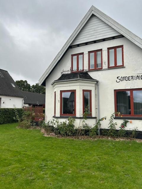a white house with red windows and a green yard at Motel Villa Søndervang 3 personers værelse in Harndrup