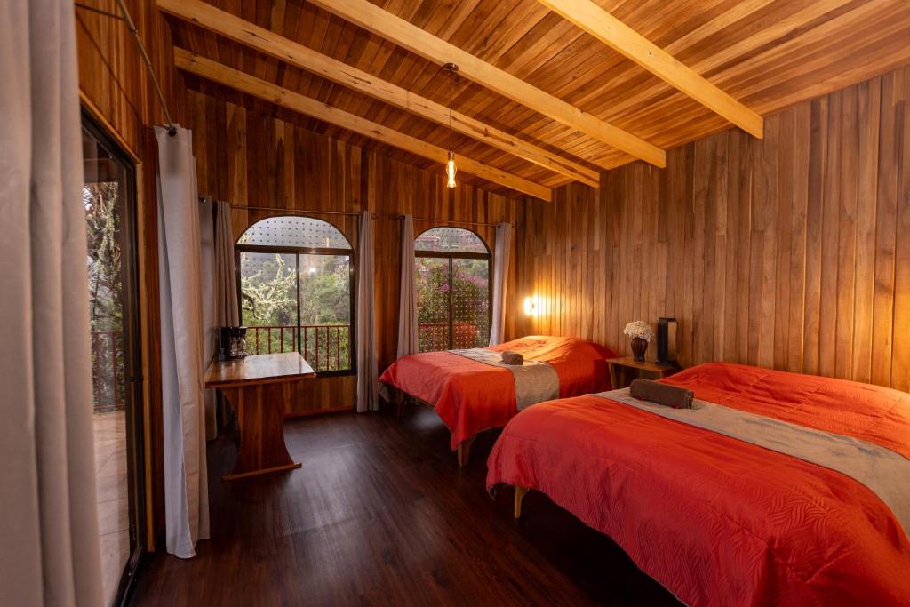 two beds in a room with wooden walls and windows at Paraíso Quetzal Lodge in Tres de Junio