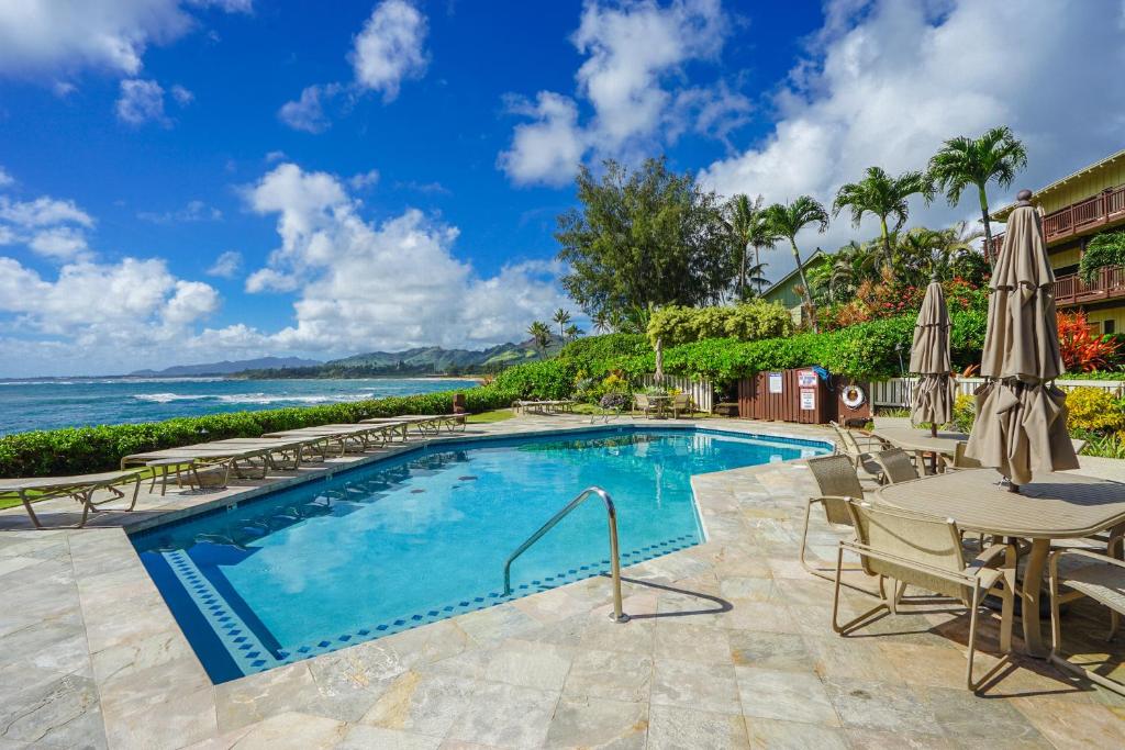 a swimming pool with tables and chairs and the ocean at Lanikai #212 in Wailua