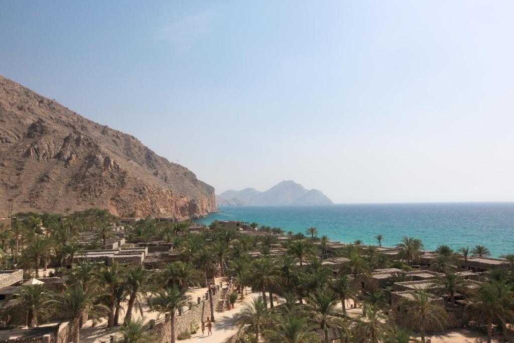 uma praia com palmeiras e o oceano em Six Senses Zighy Bay em Dibba Al-Baya